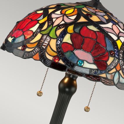 Stolová lampa s tienidlom z farebného skla zobrazuje kvetinové motívy. Tienidlo je tvorené rôznofarebnými sklenenými časťami, prevažne červenými, modrými a žltými. Lampa má čierny kovový podstavec.