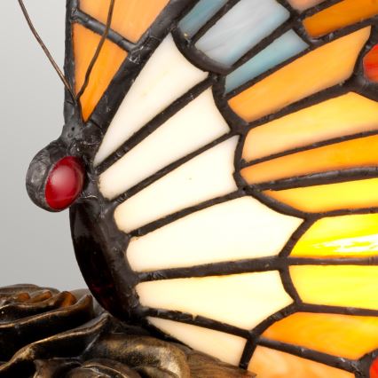 Vitrážová lampa v tvare motýľa stojí na podstavci v tvare ruže. Motýlie krídla sú zložené z farebných sklenených častí.