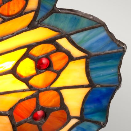 Vitrážová lampa tvaru motýľích krídel. Farebné sklo zobrazuje oranžové a žlté kvety s červenými detailmi na modrom pozadí.