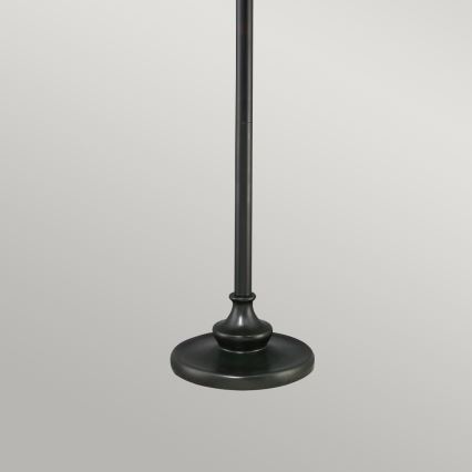 Stojanová lampa stojí na pevnej okrúhlej podstave. Jej vysoká, úzka noha je tmavo hnedá. Jednoduchý dizajn je v neutrálnom prostredí.