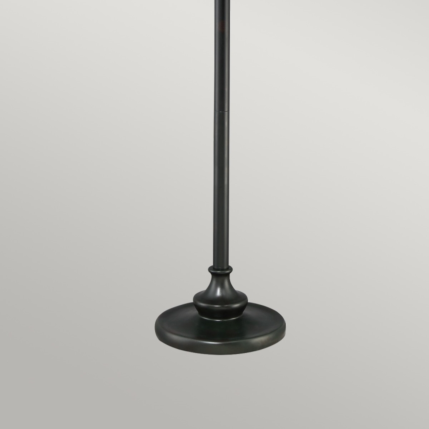 Stojanová lampa stojí na pevnej okrúhlej podstave. Jej vysoká, úzka noha je tmavo hnedá. Jednoduchý dizajn je v neutrálnom prostredí.