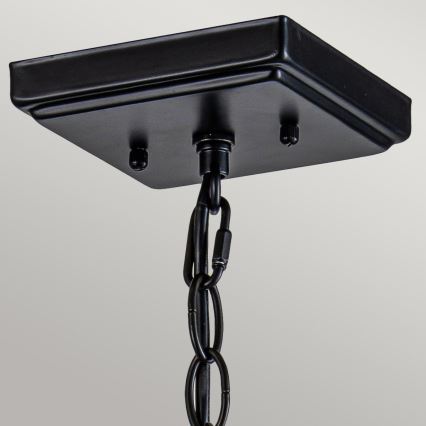 Čierny stropný držiak s pripevneným reťazom visí zo stropu. Držiak je štvorcového tvaru s tromi viditeľnými skrutkami. Reťaz je rovnako čierna.