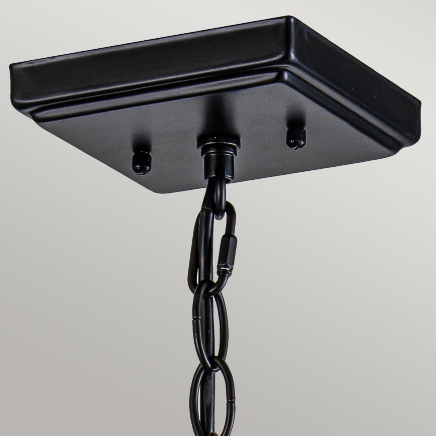 Čierny stropný držiak s pripevneným reťazom visí zo stropu. Držiak je štvorcového tvaru s tromi viditeľnými skrutkami. Reťaz je rovnako čierna.