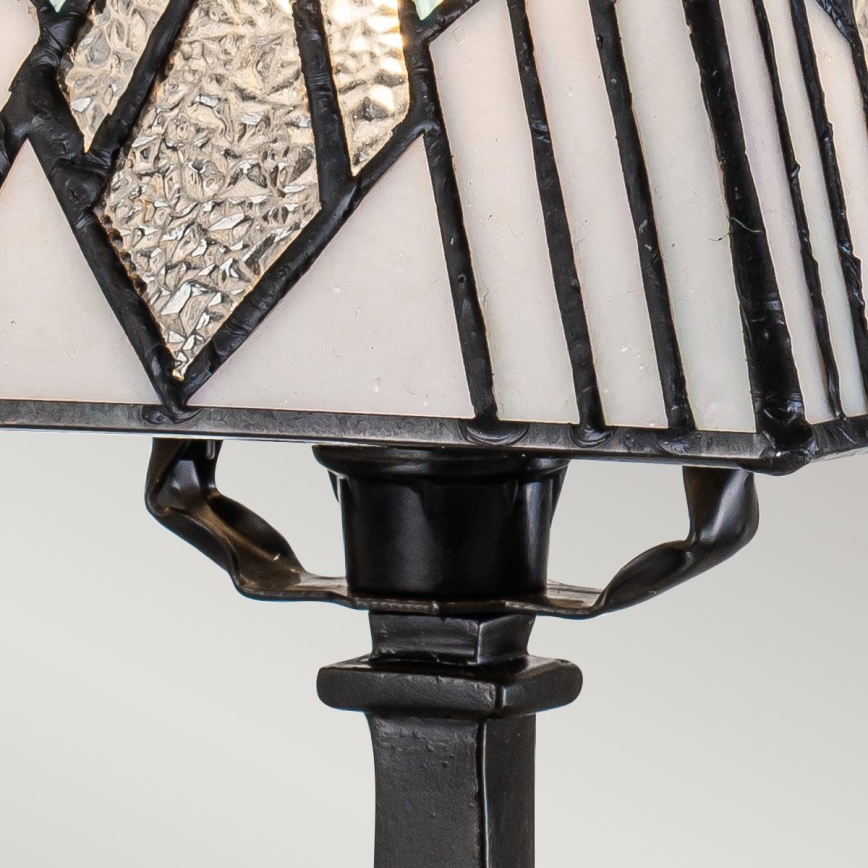 Stolová lampa s tienidlom z opálového a číreho skla s geometrickým vzorom v čierno-bielych tónoch, stojí na čiernom kovovom podstavci.