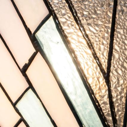 Vitrážové okno s ružovými a svetlomodrými sklenenými panelmi, spojenými čiernym kovom, presvetľuje svetlo. Štruktúra skla vytvára geometrický vzor.