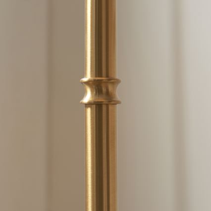 Zlatá kovová tyč s ozdobným zúžením v strede sa nachádza pred svetlou stenou.