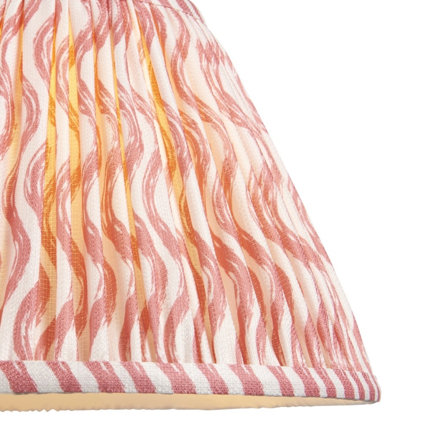 Tienidlo lampy s ružovo-bielym vlnitým vzorom je z látky s jemnými záhybmi. Spodný okraj je zdobený pruhovaným lemom. Tienidlo je osvetlené zvnútra.