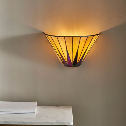 Svietidlo svieti na stene. Je to nástenné svietidlo kužeľovitého tvaru zo skla, so žltými a fialovo-purpurovými odtieňmi. Nachádza sa v miestnosti s mramorovým stolíkom.