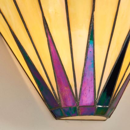 Nástenná lampa s kužeľovitým tienidlom z farebného skla vyžaruje svetlo. Tienidlo je zložené z trojuholníkových častí v odtieňoch žltej, fialovej a tmavomodrej. Lampa je pripevnená na stene.