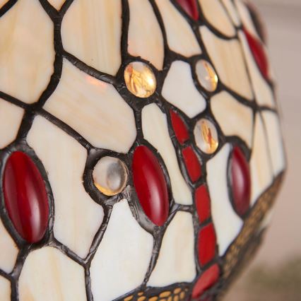 Tielňová lampa s tienidlom z farebného skla. Tienidlo je tvorené bielymi a červenými sklenými časťami, spojenými čiernou kovovou štruktúrou. Vnútorné svetlo je zapálené.