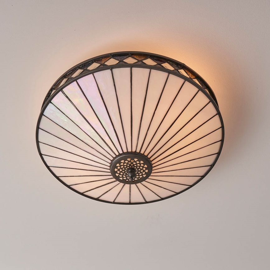 Svietidlo svieti na strope. Jeho tienidlo je okrúhle, biele, s lúčovito usporiadanými panelmi z opálového skla. Kovový rám je tmavý.