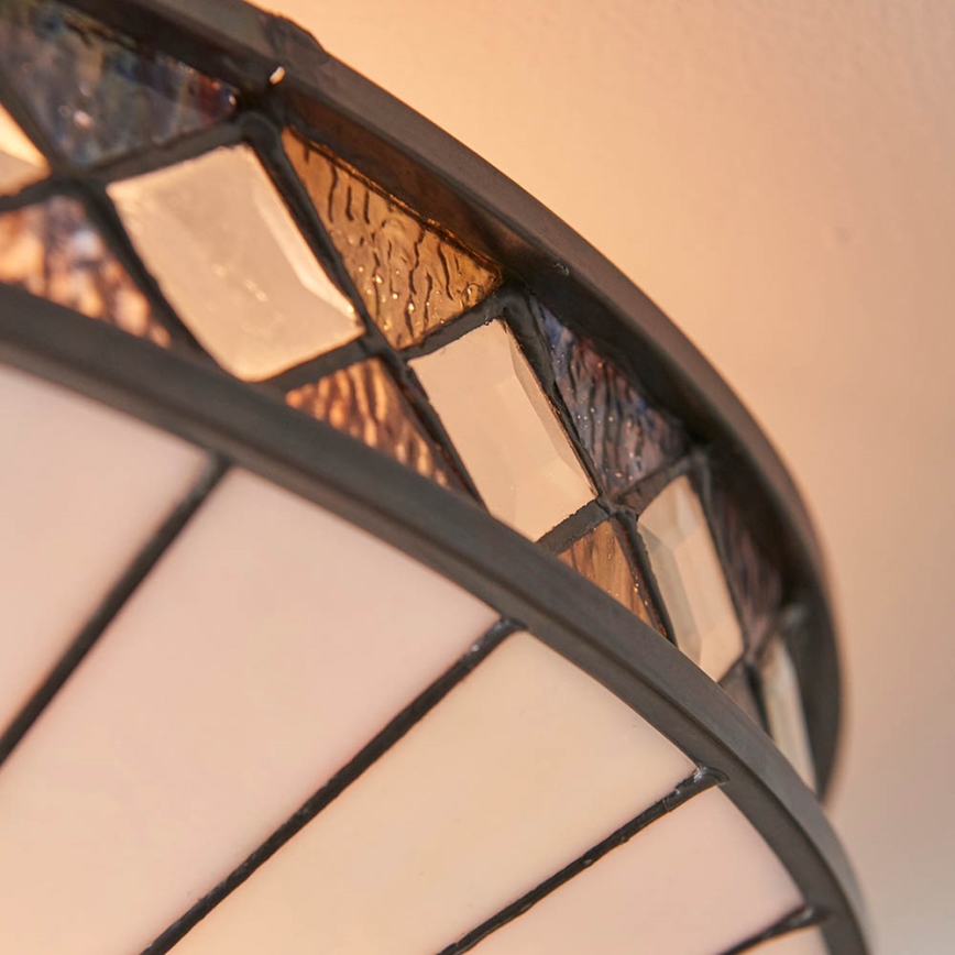 Svietidlo s okrúhlym tienidlom je zhotovené z farebného skla v hnedých, béžových a priesvitných odtieňoch, usporiadaných do geometrických tvarov. Tienidlo je orámované tmavohnedým kovom. Svietidlo je inštalované v interiéri, pripevnené k stropu.