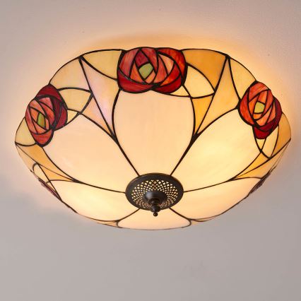 Svietidlo s vitrážovým tienidlom v tvare kvetu s červenými a krémovými ružami svieti pripevnené k stropu.