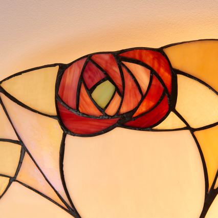 Vitrážové svetlo zobrazuje červenú ružu zloženú z farebných sklenených častí. Svetlo je čiastočne podsvietené, čím vytvára teplý odtieň. V pozadí je viditeľná krémová farba pozadia.