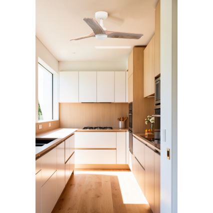 Stropný ventilátor s drevenými lopatkami sa otáča v modernej kuchyni s drevenou a bielou kuchynskou linkou a svetlou drevenou podlahou.