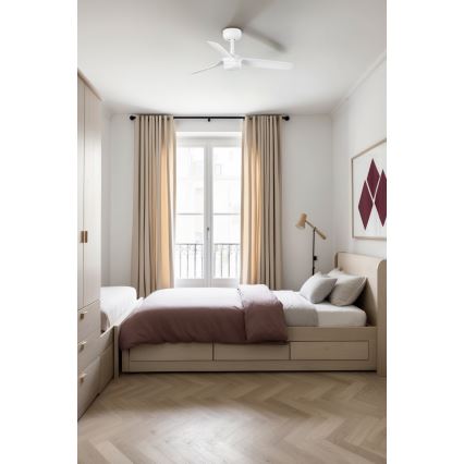 Biely stropný ventilátor sa nachádza v spálni. Ventilátor je umiestnený nad posteľou s úložným priestorom, ktorá stojí na svetlej drevenej podlahe s rybinovou dlažbou. V miestnosti sú svetlé závesy a vstavaná skriňa.