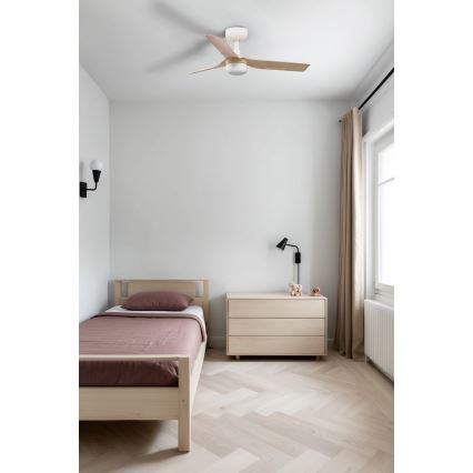 Stropný ventilátor s drevenými lopatkami sa otáča v detskej izbe. Izba má posteľ, komodu a svetlé drevené podlahy.