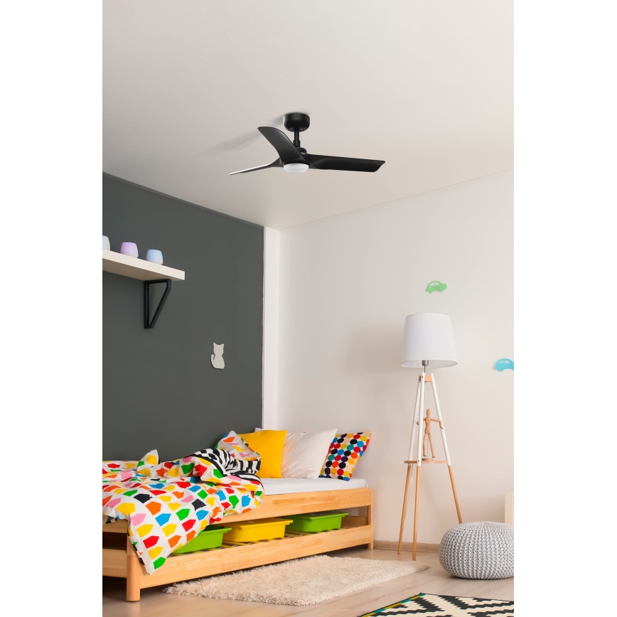 Čierny stropný ventilátor s integrovaným osvetlením je pripevnený na strope detskej izby. V miestnosti sa nachádza posteľ s farebnou posteľnou bielizňou a doplnkami.