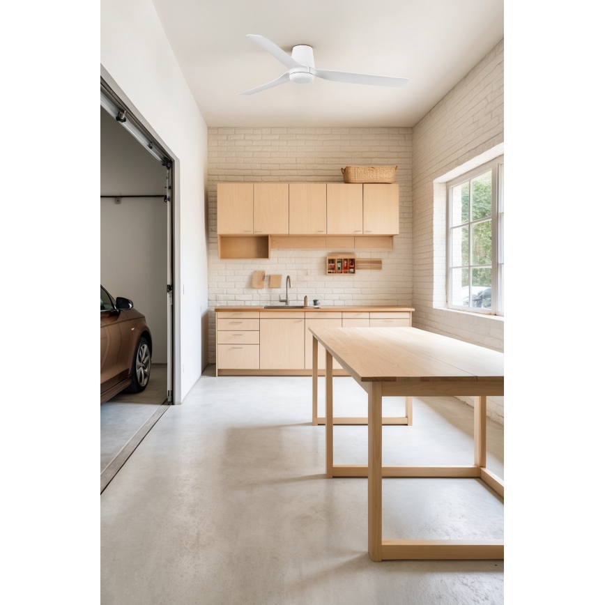 Biely stropný ventilátor rotuje v svetlej miestnosti s dreveným nábytkom. Miestnosť má kuchynskú linku, drevený stôl, betónovú podlahu a výhľad do garáže s autom.