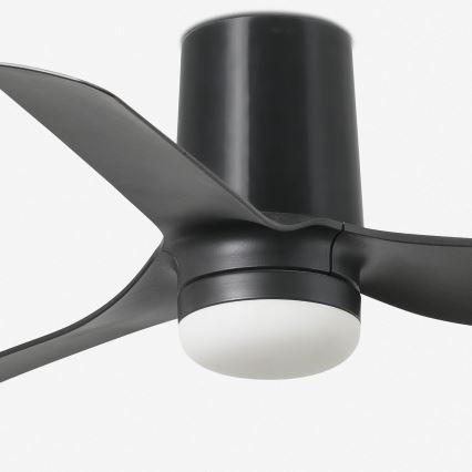 Čierny stropný ventilátor s tromi lopatkami sa otáča. Má zabudované svetlo s bielym difúzorom. Je umiestnený na bielom pozadí.