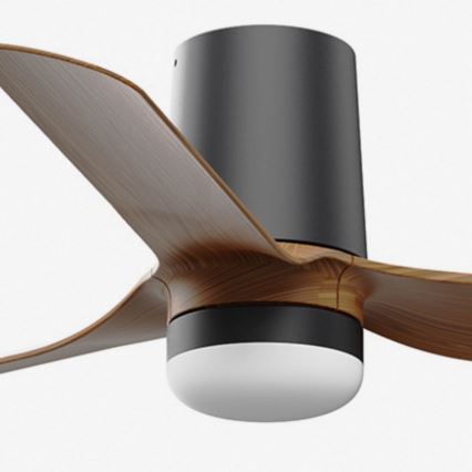 Stropný ventilátor s drevenými lopatkami sa otáča. Má čierny stĺpik a integrované svetlo. Na pozadí je čisté biele pozadie.