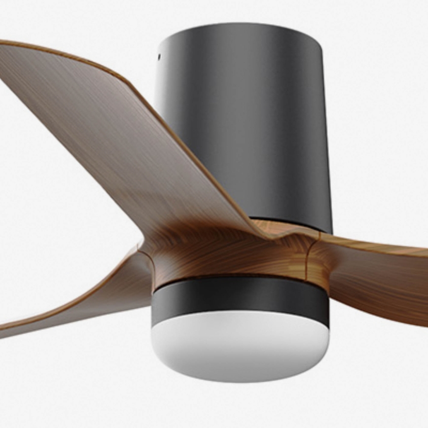 Stropný ventilátor s drevenými lopatkami sa otáča. Má čierny stĺpik a integrované svetlo. Na pozadí je čisté biele pozadie.