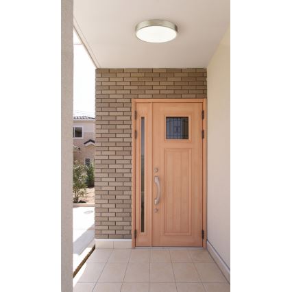 Dvere z svetlého dreva sa nachádzajú v exteriéri domu. Dvere sú osadené v tehlovej stene. Nad dverami je stropné svietidlo.