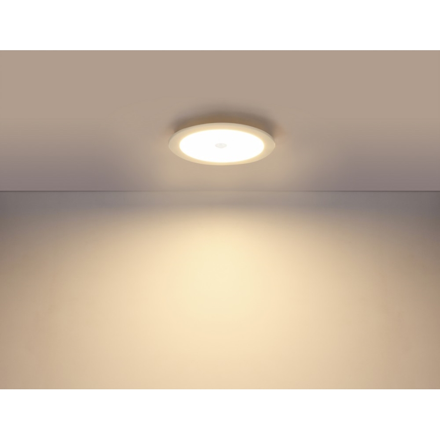 Okrúhle LED svetlo svieti na svetlohnedú stenu zo stropu. Svetlo je zapnuté a vytvára jemné osvetlenie.