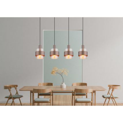 Štyri medené závesné svietidlá s priehľadnými sklenenými prvkami visia nad dreveným jedálenským stolom so stoličkami v jedálni.