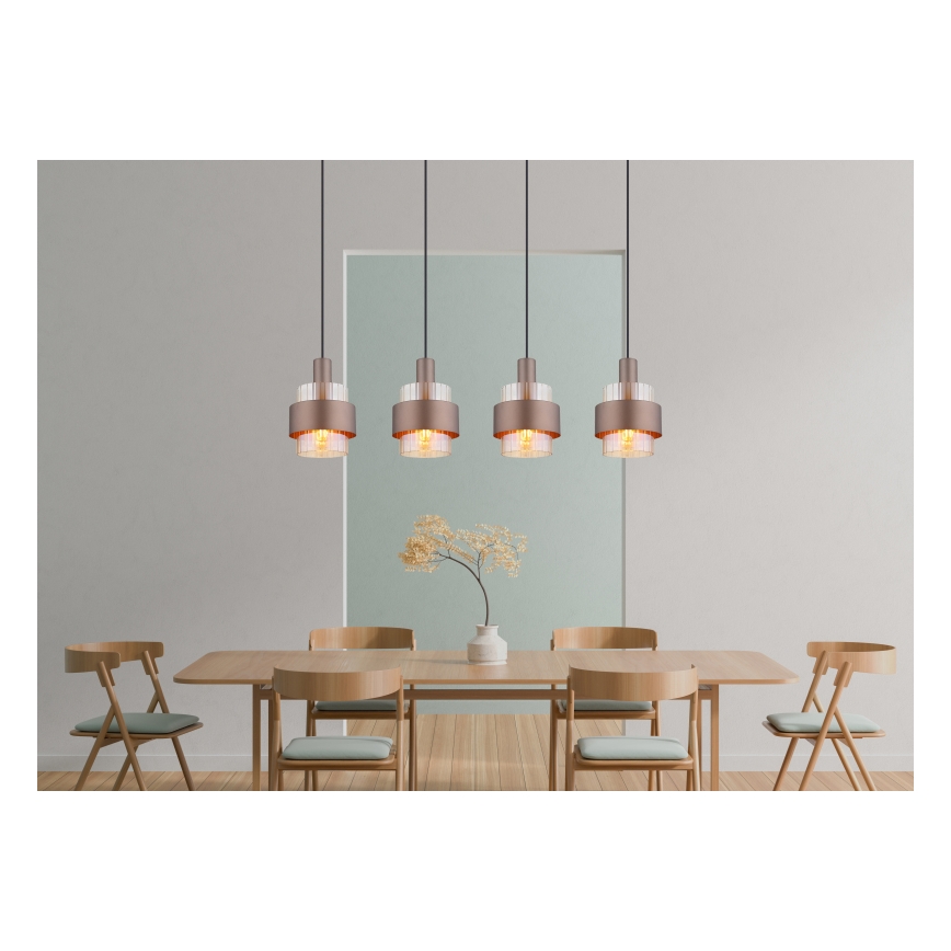 Štyri medené závesné svietidlá s priehľadnými sklenenými prvkami visia nad dreveným jedálenským stolom so stoličkami v jedálni.