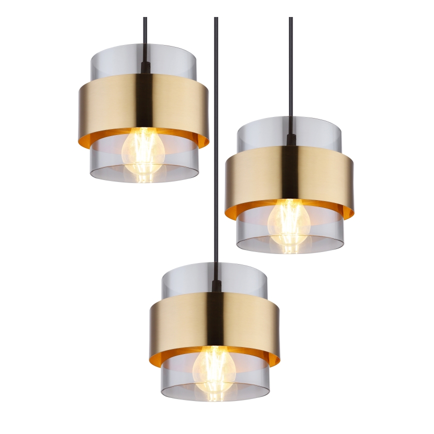 Tri závesné lampy visia zhora. Každá lampa má zlatý kovový pás a priehľadný sklenený valec s vnútornou žiarovkou. Lampa je zavesená na čiernom kábli na bielom pozadí.