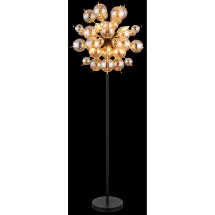 Stojacia lampa s vysokým čiernym stojanom a rozsiahlym tienidlom zloženým z mnohých malých, priesvitných sklenených guličiek jantárovej farby. Guličky sú pripevnené k centrálnemu bodu a vytvárajú rozvetvený tvar.