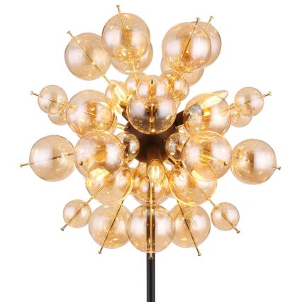 Stojacia lampa svieti. Je zložená z mnohých malých, guľových, jantárových sklenených tienidiel pripevnených na čiernej kovovej konštrukcii. Tienidlá sú osvetlené žiarovkami.