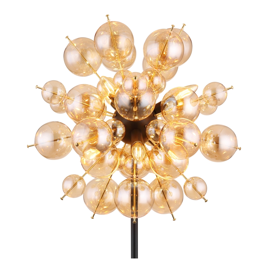 Stojacia lampa svieti. Je zložená z mnohých malých, guľových, jantárových sklenených tienidiel pripevnených na čiernej kovovej konštrukcii. Tienidlá sú osvetlené žiarovkami.