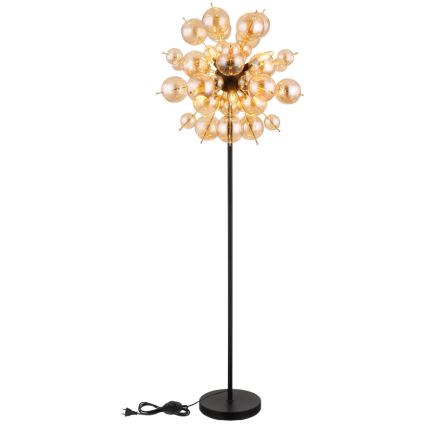 Stojacia lampa s čiernou kovovou nohou a tienidlom z viacerých malých, priesvitných, hnedo-zlatých sklenených gúľ, svieti na bielom pozadí.