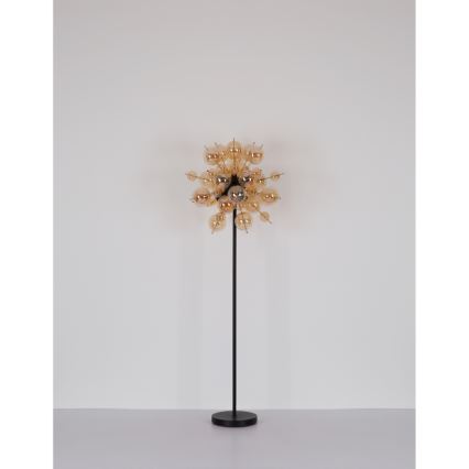 Stojacia lampa s vysokým čiernym stojanom a svietidlom zloženým z viacerých malých jantárových sklenených guľôčok usporiadaných v tvare rozvetveného kvetu pred bielou stenou.