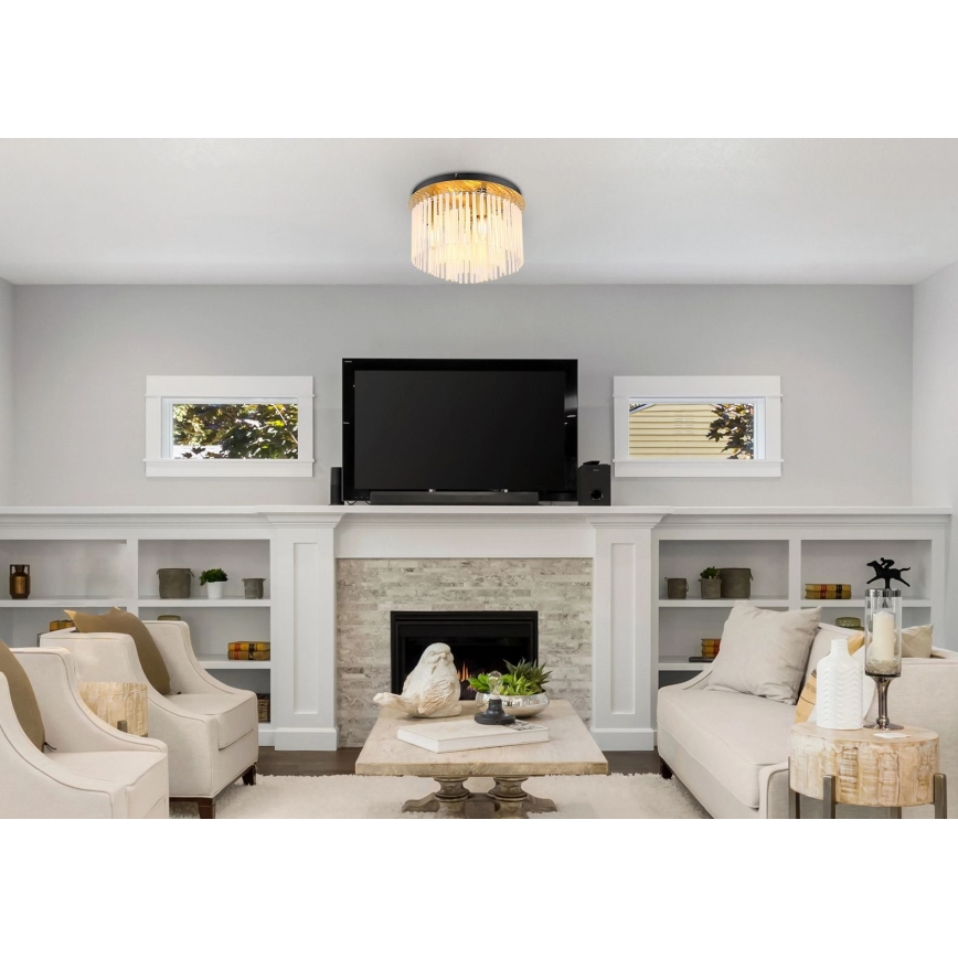 Stropné svietidlo svieti v obývacej izbe. Svietidlo má čierny okrúhly rám a visiace sklenené tyčinky. Izba obsahuje pohovku, kreslá, televízor a krb.