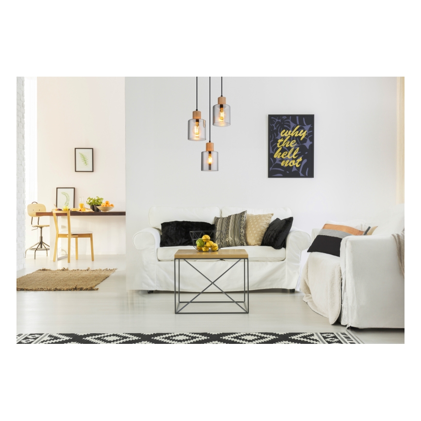 Trojica sklenených závesných lámp s drevenými prvkami visí v obývacej izbe nad bielym gaučom a konferenčným stolíkom. Na stene visí obraz s nápisom „why the hell not“.