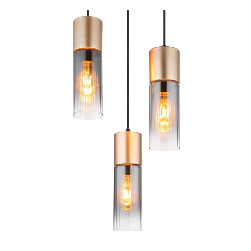 Tri visiace lampy s valcovými tienidlami z priehľadného ryhovaného skla a zlatými kovovými prvkami visia na čiernych kábloch pred bielym pozadím. Lampy obsahujú žiarovky.