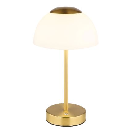 Stolová lampa s bielym tienidlom v tvare kupoly a zlatou kovovou základňou a stonkou. Lampa svieti. Je umiestnená na bielom pozadí.