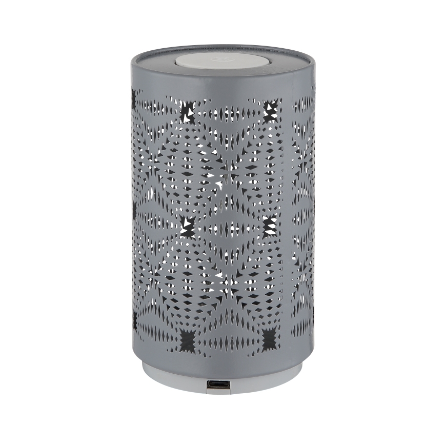 Šedá valcová lampa s vyrezávaným vzorom stojí na bielom pozadí. Spodná časť obsahuje USB port.