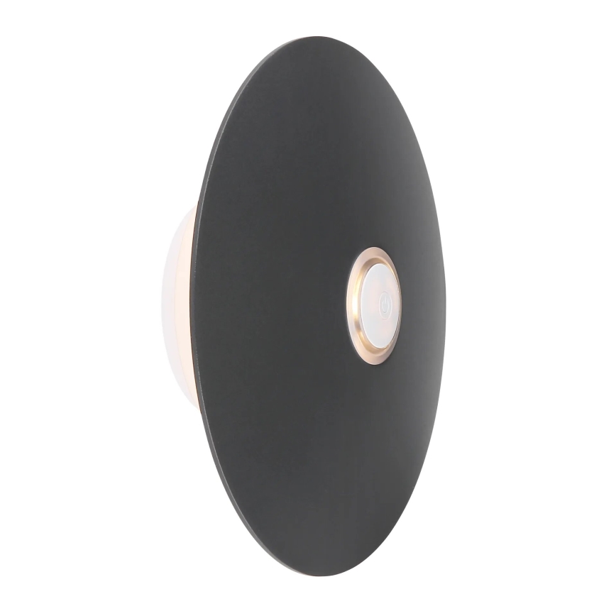 Nástená lampa svieti. Je tmavosivá, okrúhla, plochá, s malým svetlým vypínačom v strede. Upevnená je na stene.
