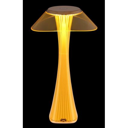Žltá stolová lampa v tvare huby svieti. Jej noha má ryhovaný povrch. Lampa je umiestnená na tmavom pozadí.