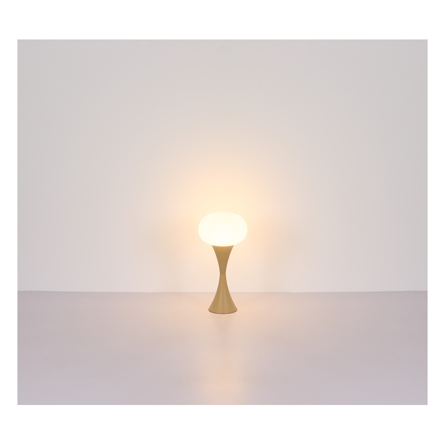 Stolná lampa s guľovou tienidlom svieti. Tienidlo je biele, stojan béžový. Lampa stojí na svetlej ploche pred svetlou stenou.