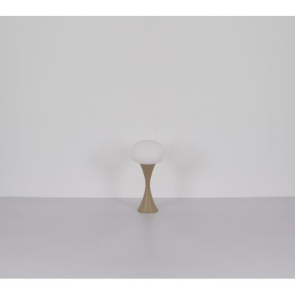 Stolová lampa stojí na svetlej podlahe pred svetlou stenou. Lampa má guľovitý biely tienidlo a hnedý kovový podstavec v tvare tulipánu.