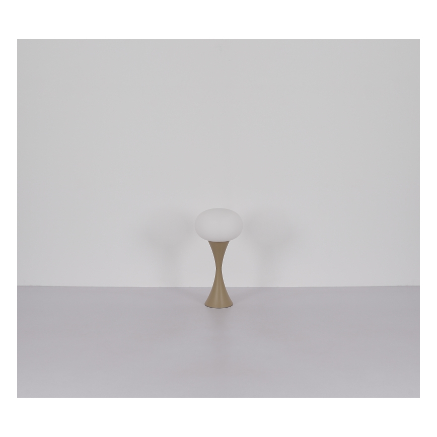 Stolová lampa stojí na svetlej podlahe pred svetlou stenou. Lampa má guľovitý biely tienidlo a hnedý kovový podstavec v tvare tulipánu.