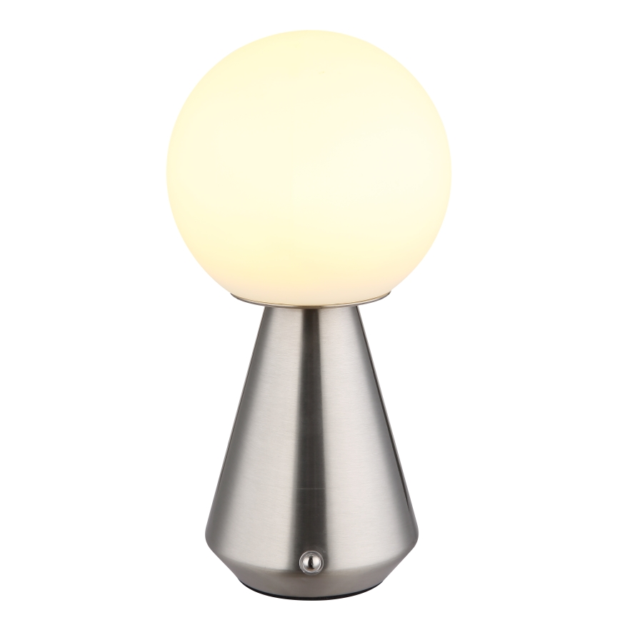 Stolová lampa svieti. Guľová, mliečne biela vrchná časť je umiestnená na kužeľovitom, striebornom podstavci s vypínačom.
