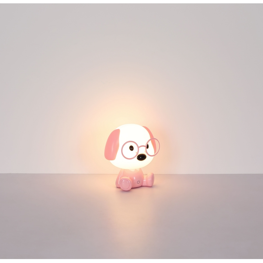 Ružová stolná lampa v tvare psa s okuliarmi svieti na svetlomodrej podlahe pred svetlou stenou.