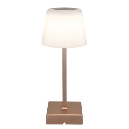 Stolová lampa svieti. Má valcovitý tienidlo z matného bieleho materiálu a kovový podstavec a stĺpik v medenom odtieni. Lampa stojí na štvorcovej základni.