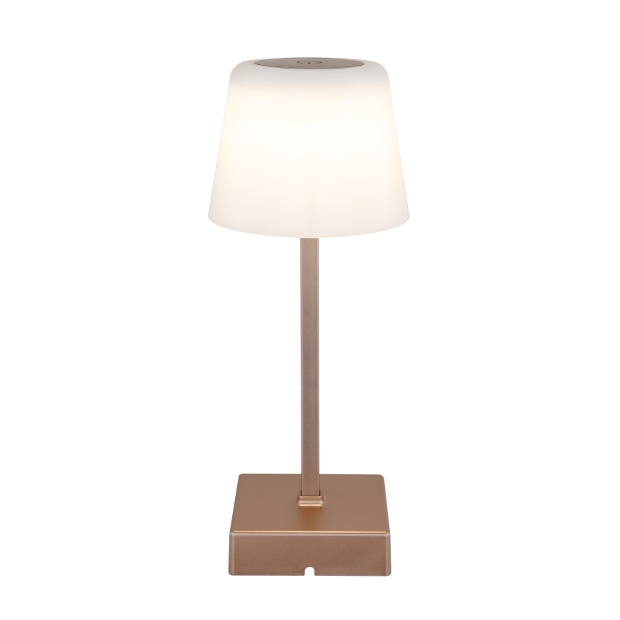 Stolová lampa svieti. Má valcovitý tienidlo z matného bieleho materiálu a kovový podstavec a stĺpik v medenom odtieni. Lampa stojí na štvorcovej základni.